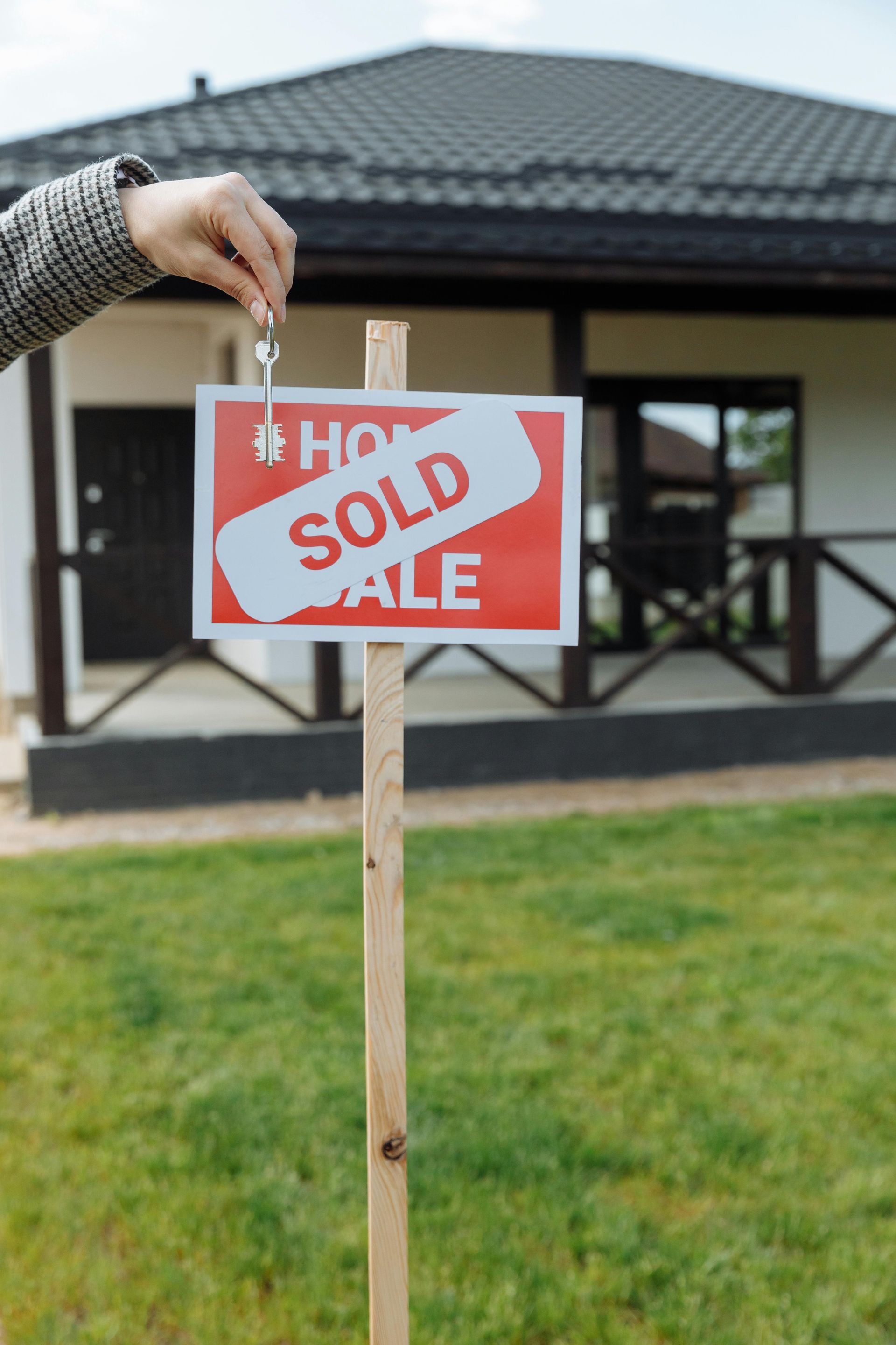 Hand placing a red sold sign on a post in front of a house