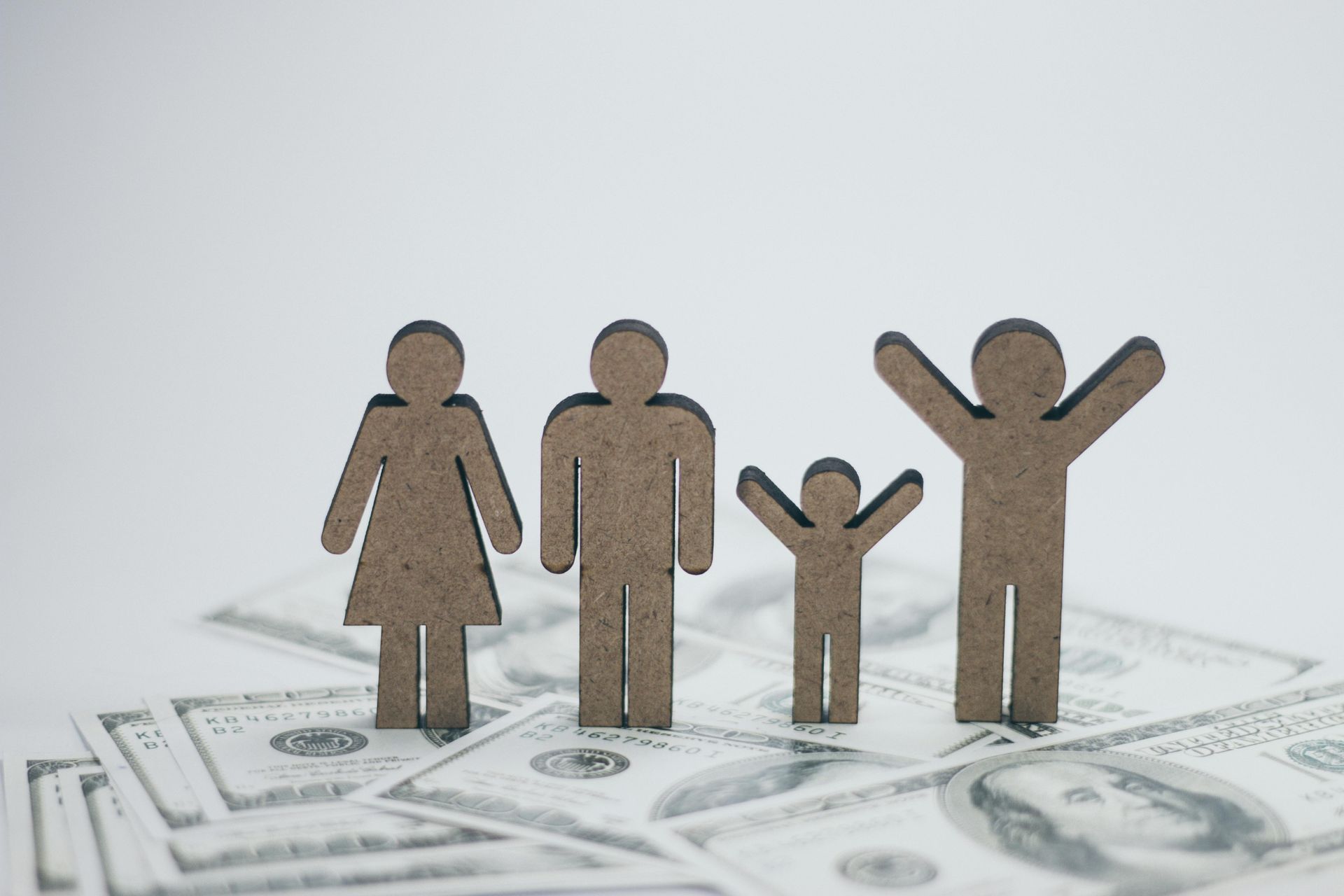 Paper cutout family figures standing on dollar bills, symbolizing household finances and savings.