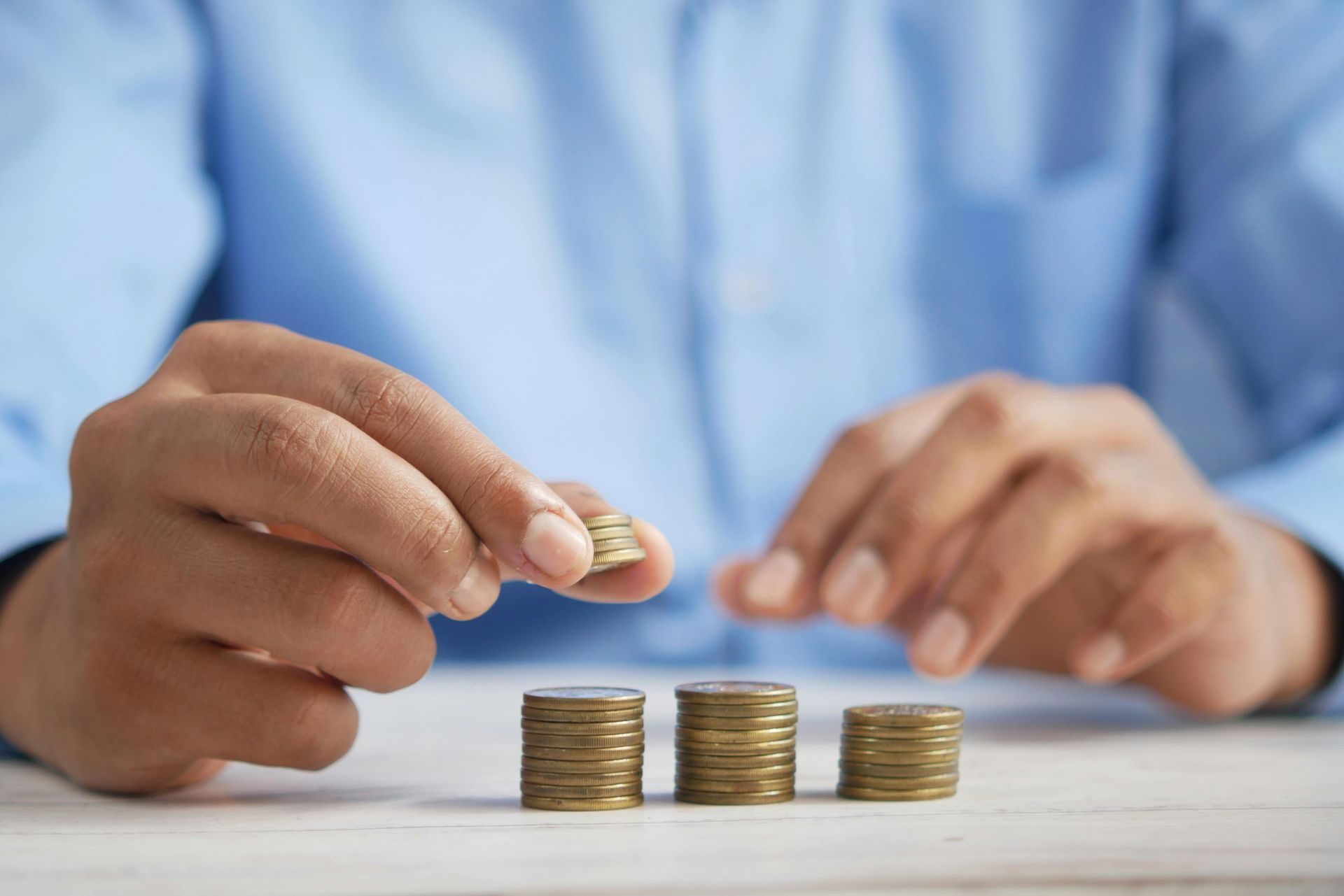 Hands stacking coins on a table beside a person in a blue shirt