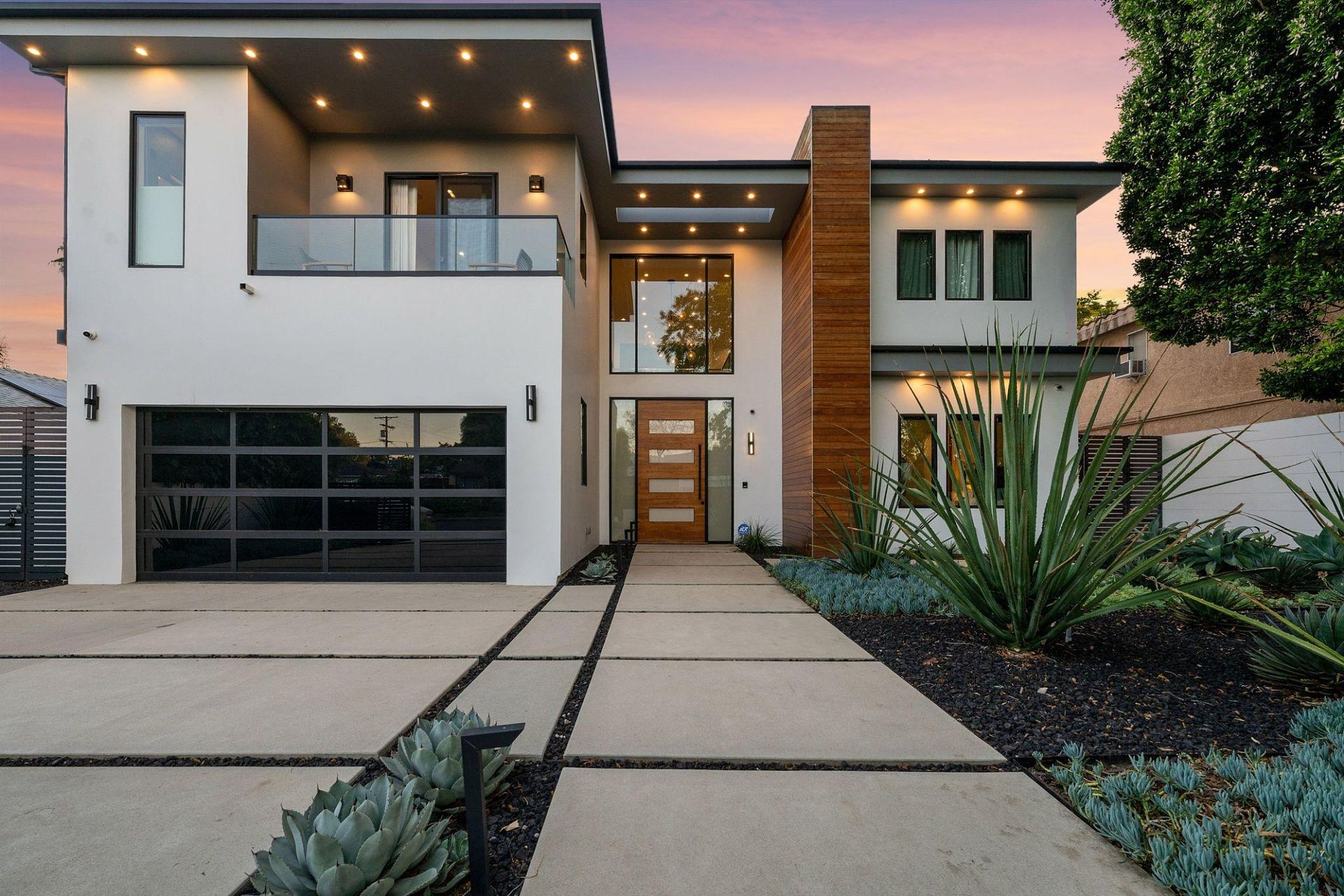 Modern two-story house exterior with a driveway, front walkway, and lit porch at dusk