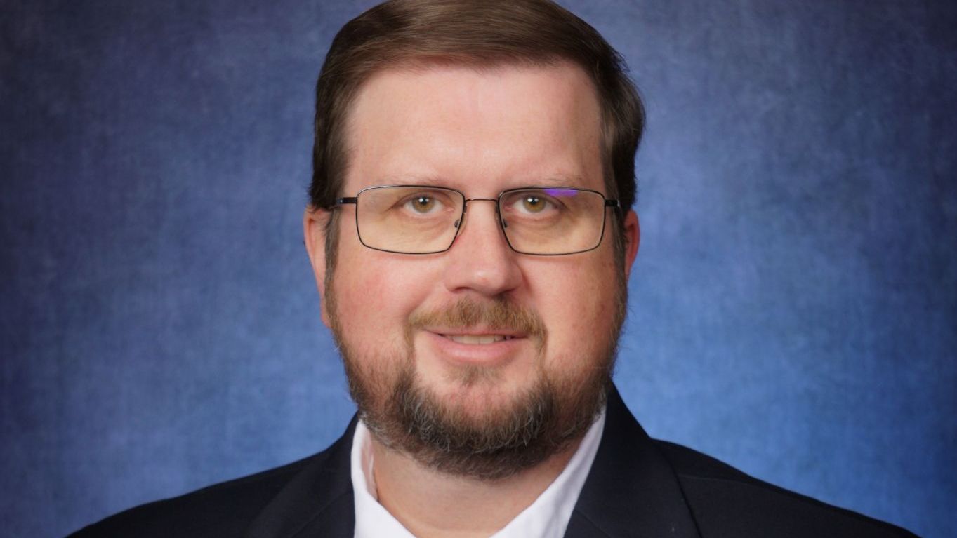 A man with a beard and glasses is wearing a suit and tie.