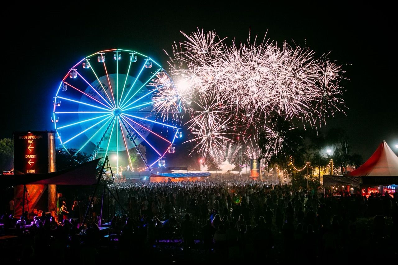 A ferris wheel is lit up at night with fireworks in the background.