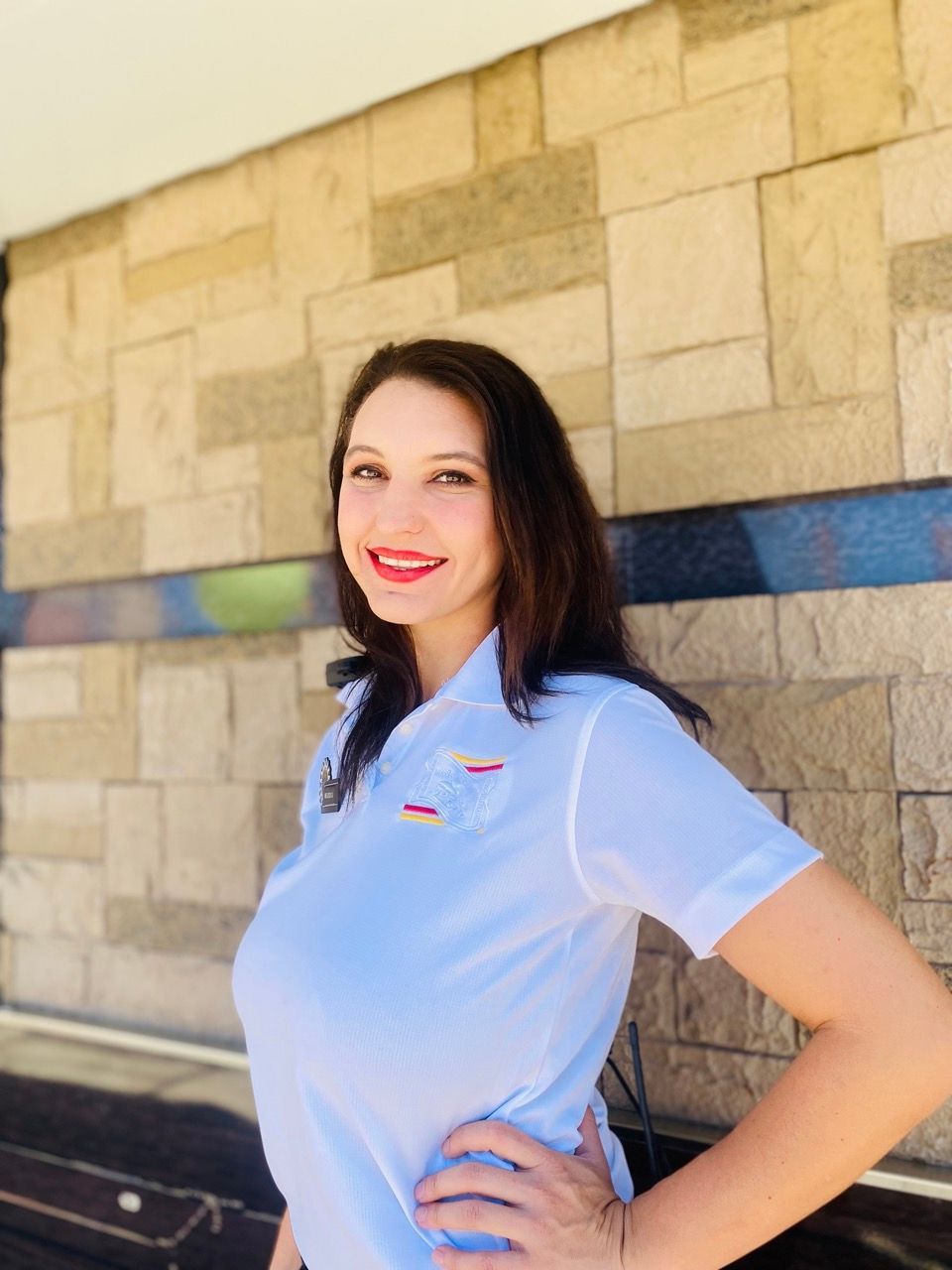 A woman in a white shirt is standing in front of a brick wall.