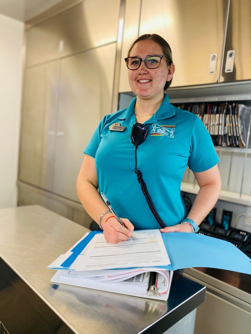 Staz standing at a counter holding a clipboard and smiling.