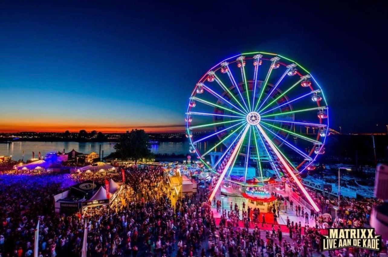 A crowd of people are gathered around a ferris wheel at night.