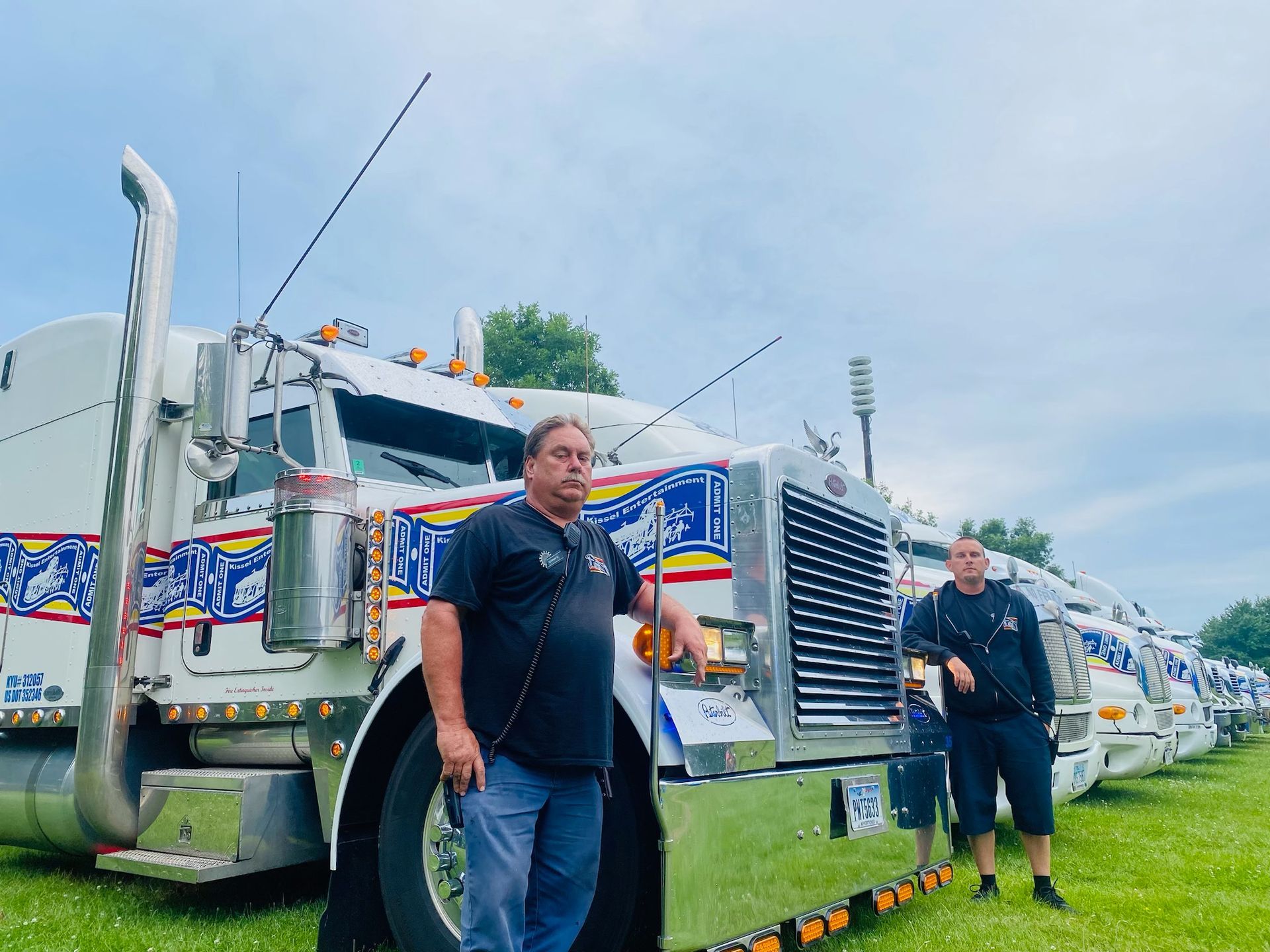 Two men are standing in front of a row of semi trucks.