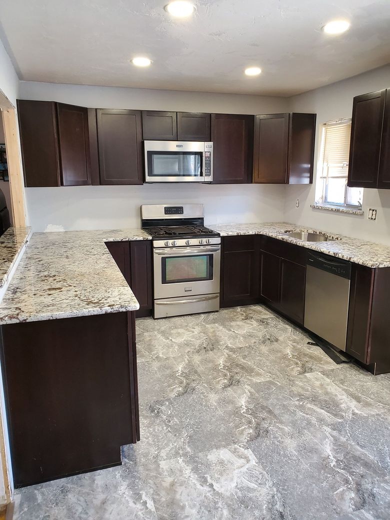 Modern kitchen with dark brown cabinetry, granite countertops, stainless steel appliances, and tile flooring.