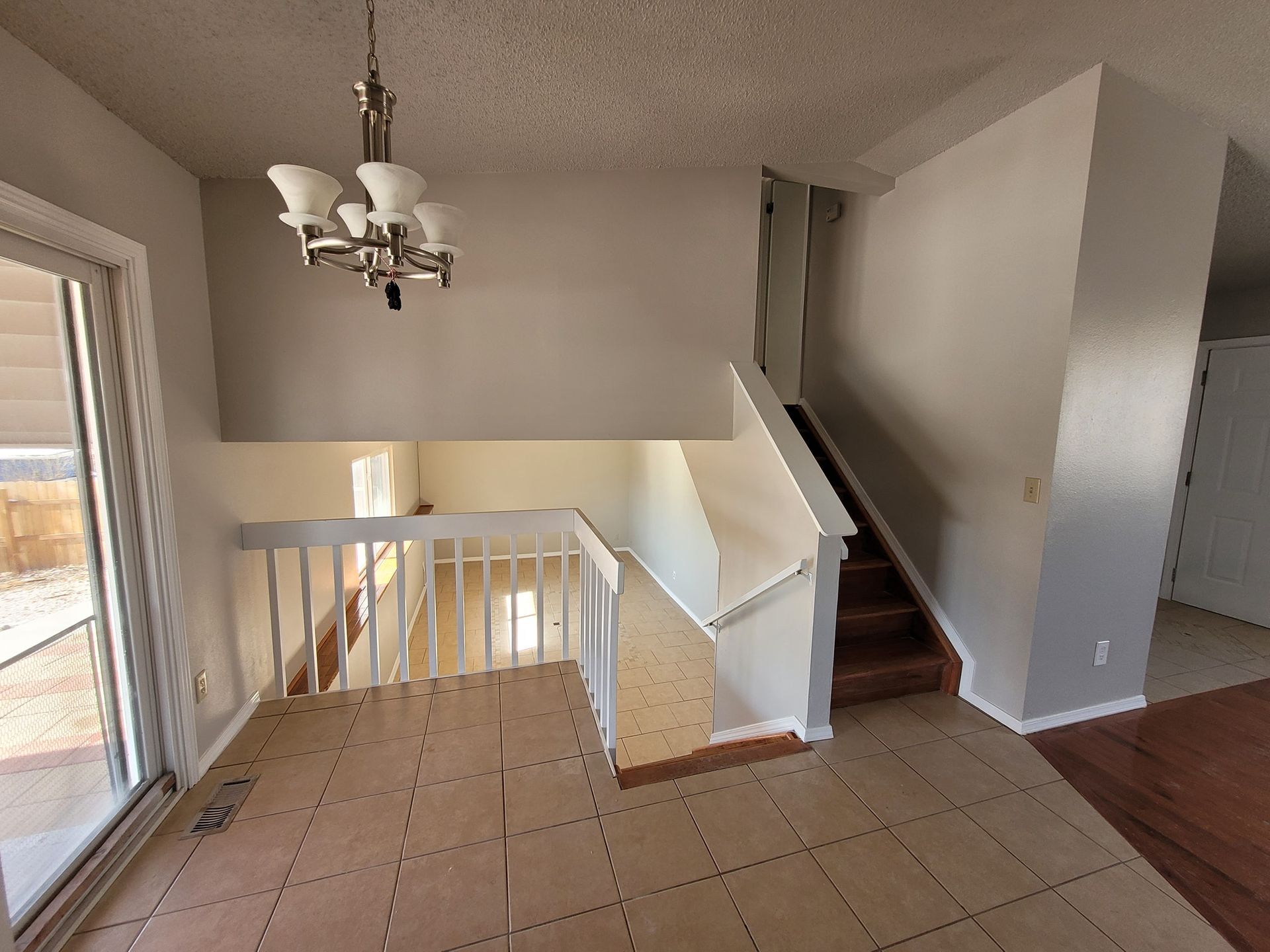 A split-level interior featuring a tiled entryway, a staircase with white railings, and a hanging chandelier.