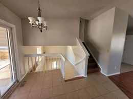 A split-level interior featuring a tiled entryway, a staircase with white railings, and a hanging chandelier.