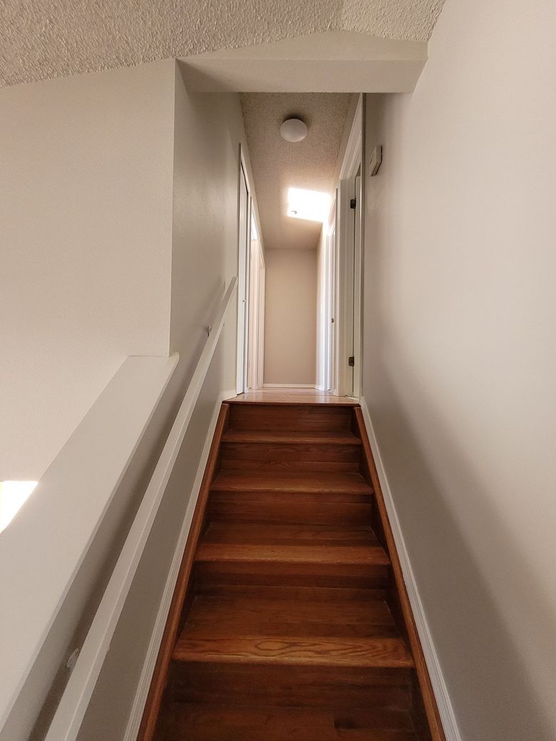 A set of wooden stairs leads upward to a narrow hallway with white walls and a ceiling light.