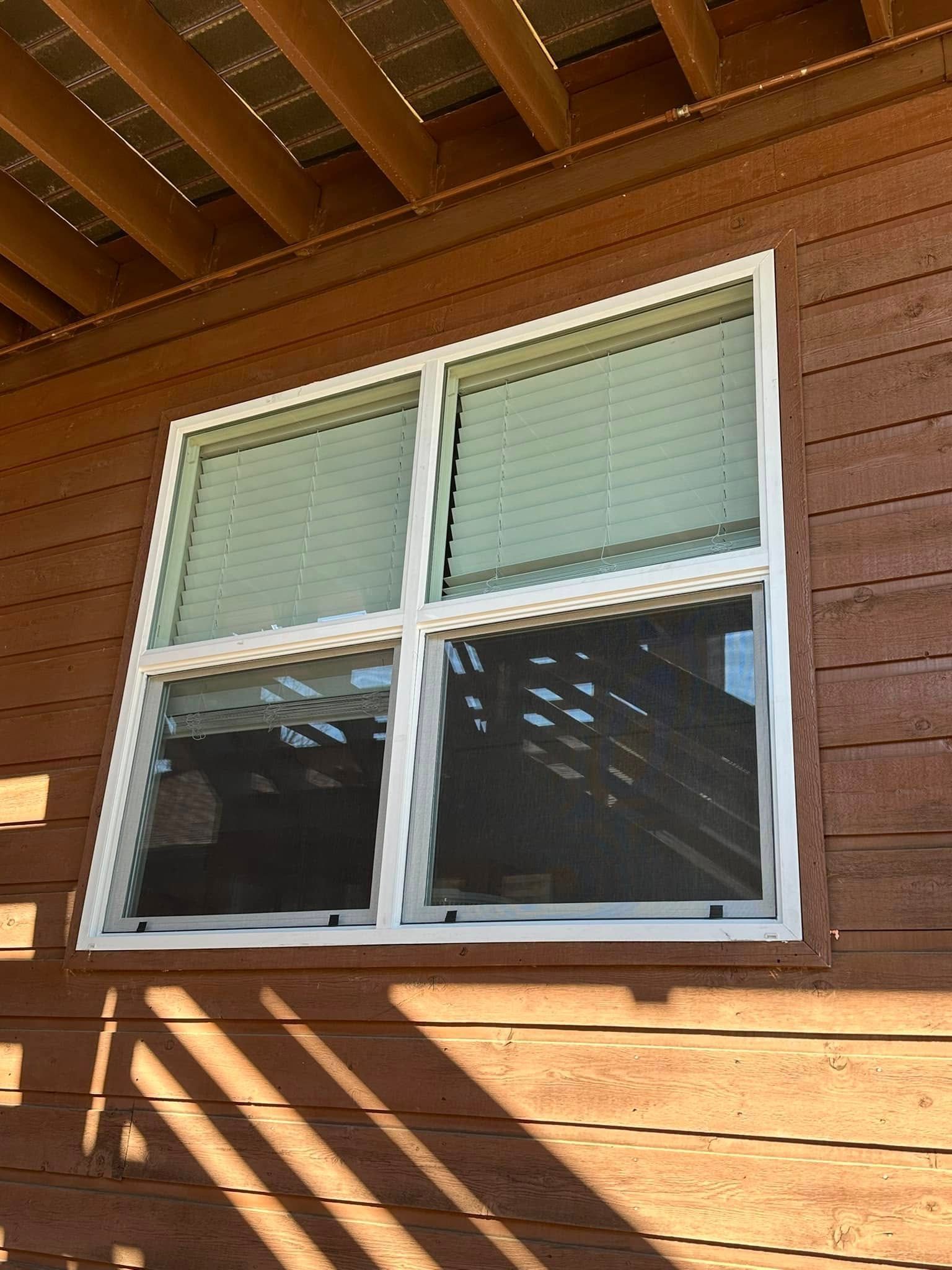 A square white-framed window with a horizontal grid on a wooden exterior wall, partially shaded by overhead structure.