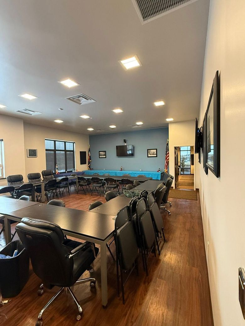 A U-shaped conference table with black chairs in a brightly lit room with a blue accent wall and wooden floors.