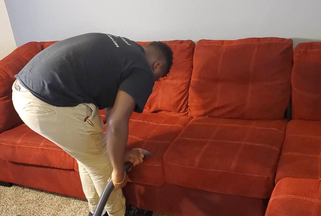 Person vacuuming a red couch in a room.