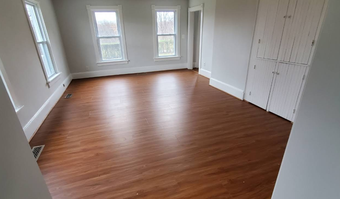 Empty room with wood-look flooring, two windows, and white trim. Gray walls and white closet doors.