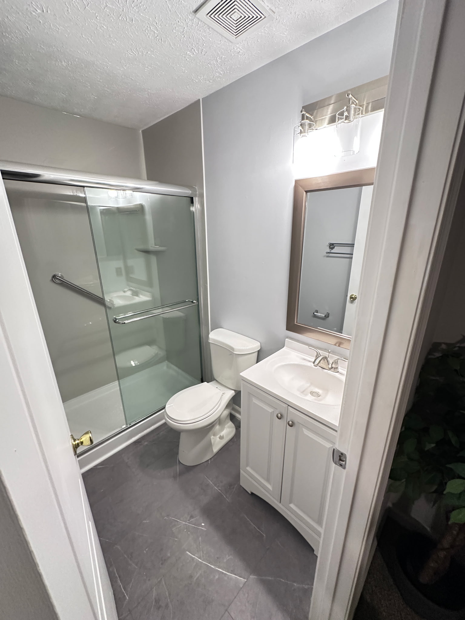 Bathroom with gray walls, glass shower, white vanity, and gray floor tiles.