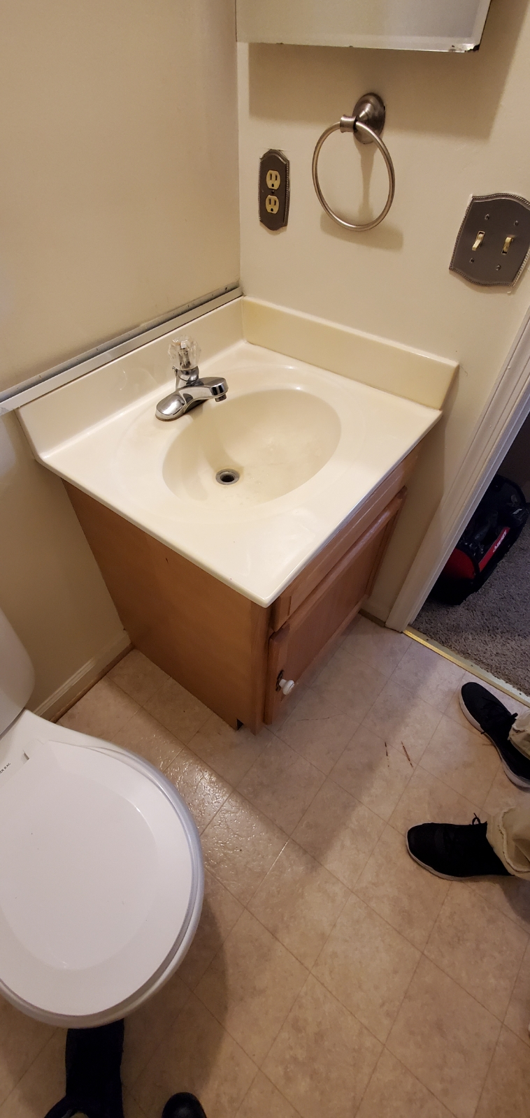 A small bathroom with a sink, toilet, and cabinet, in a home. The floors are yellow-beige.