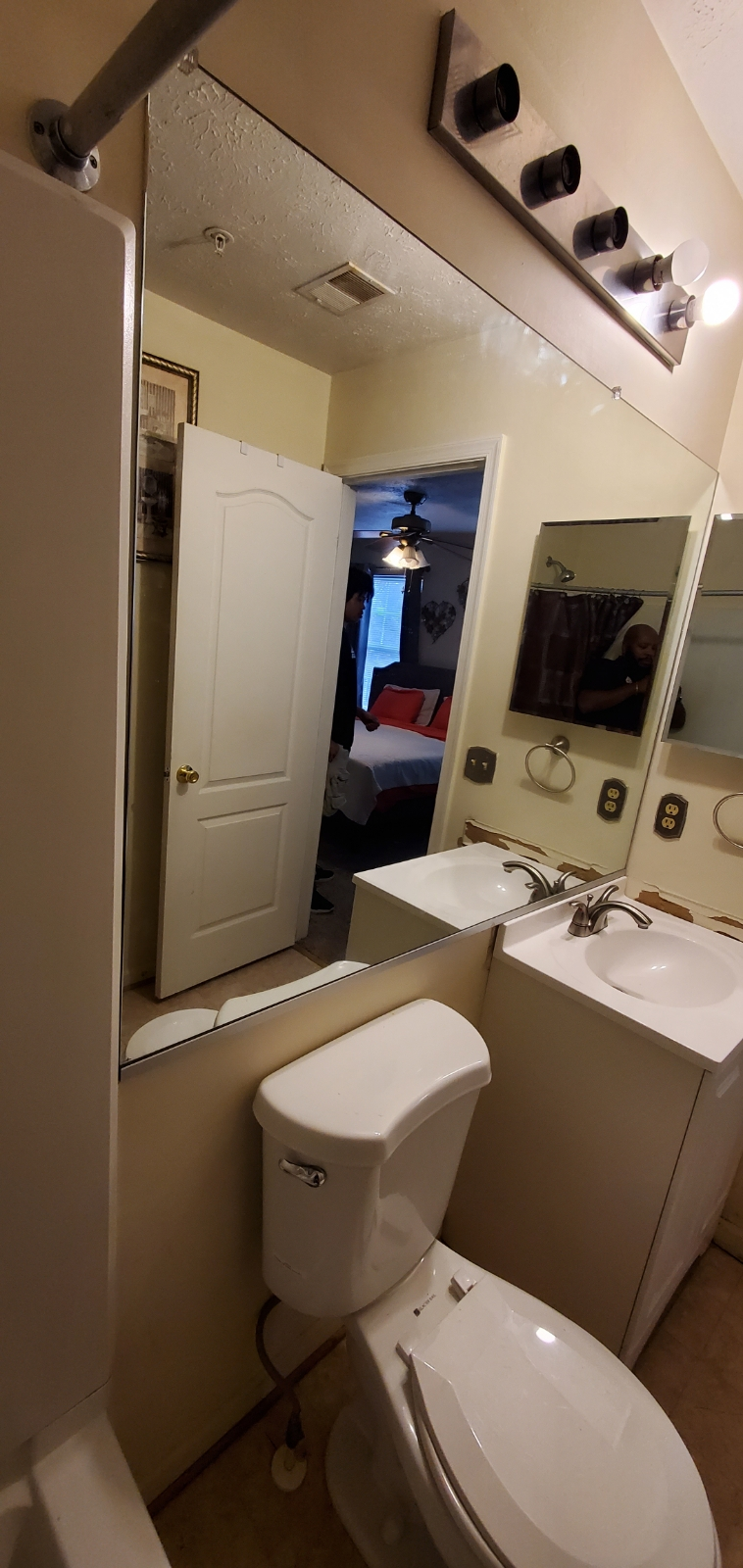 Bathroom with a toilet, vanity, and large mirror reflecting another room with a door.