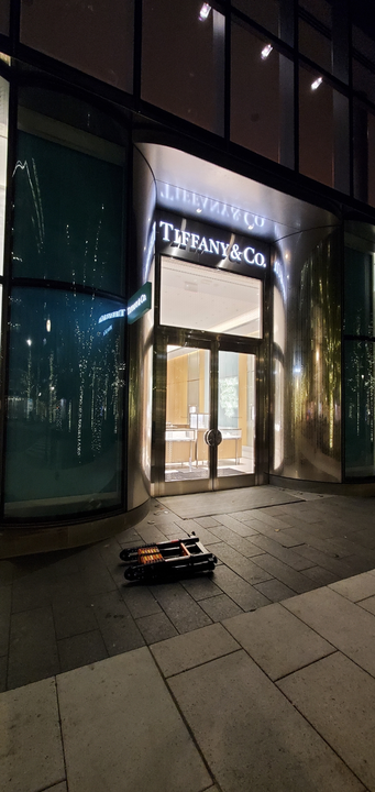 Exterior of a Tiffany & Co. store at night. A folded-up luggage cart sits on the sidewalk in front of the entrance.