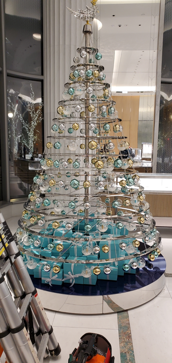A spiral, silver Christmas tree with turquoise and gold ornaments. At the base are small gift boxes.