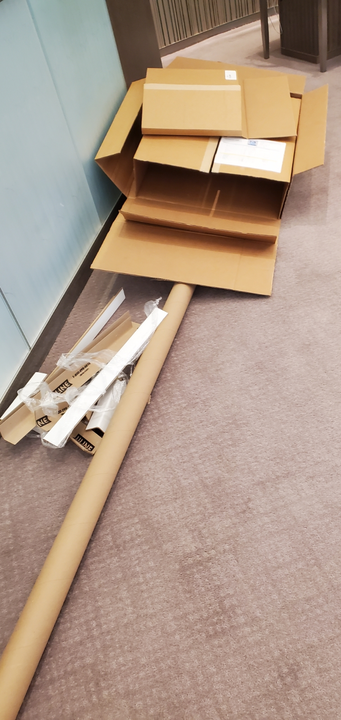 Cardboard boxes and packing materials on a carpeted floor, near a wall.