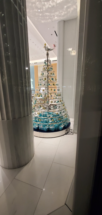 A modern art Christmas tree with blue and clear ornaments, inside a building.