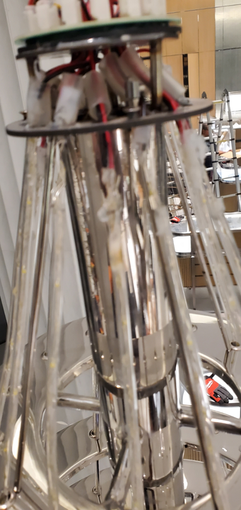 A metallic structure with a cylindrical body and supporting struts. Wires and components are visible at the top.