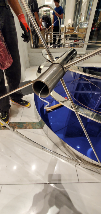 Workers constructing a modern sculpture with blue panels and stainless steel tubes.