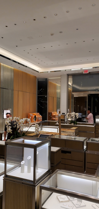 Inside a jewelry store with display cases, employees, and decorative orchids.