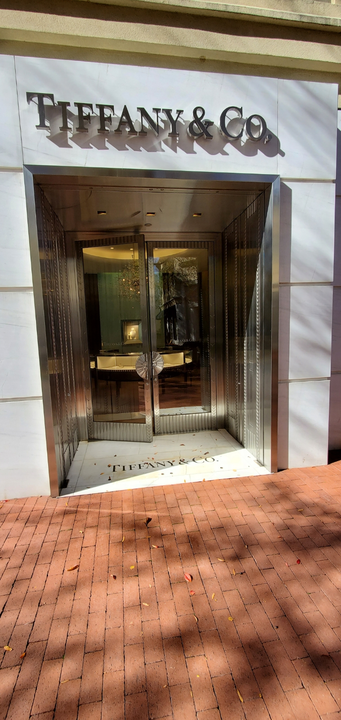 Tiffany & Co. store entrance with silver doors and signage. Red brick pavement in front.
