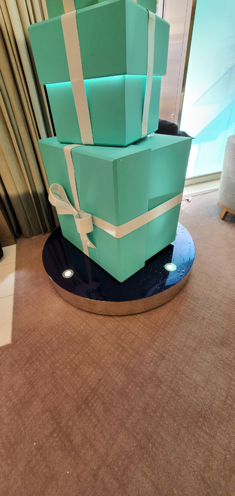 Stacked teal gift boxes with white ribbon on a round, shiny, dark surface.
