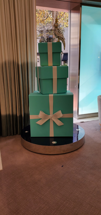 A tiered cake resembling gift boxes in Tiffany blue with white bows, topped with a golden bird.