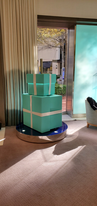 Three Tiffany & Co. gift boxes stacked on a circular platform. Turquoise boxes with white ribbon. Indoors.