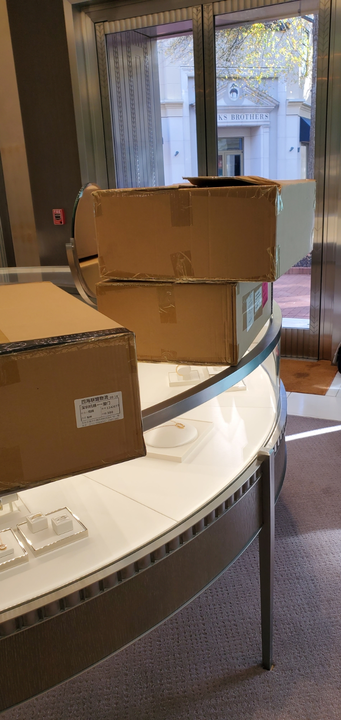 Cardboard boxes stacked on a display counter inside a store, near glass doors.