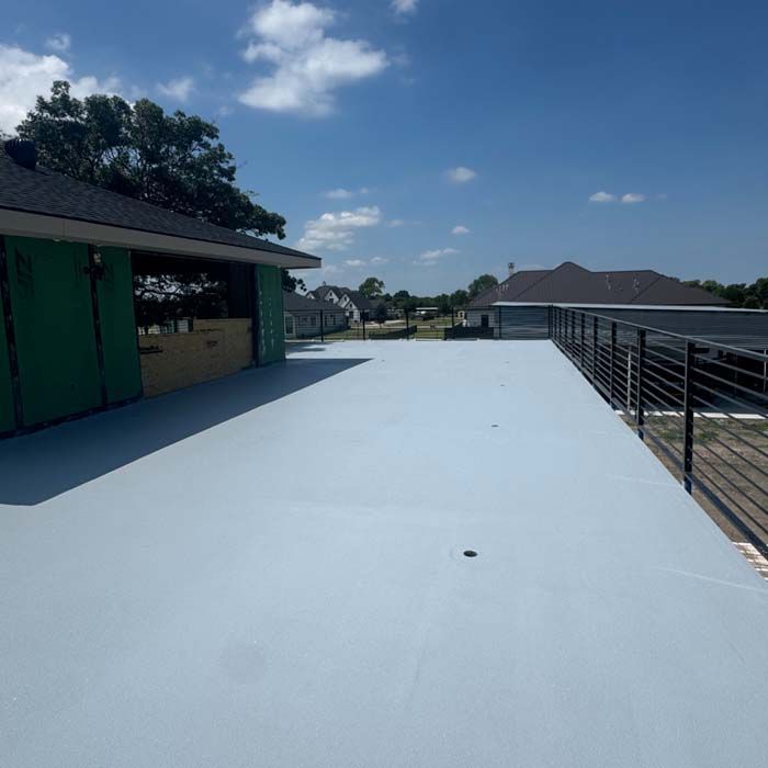 A flat, light gray rooftop with black railing and blue sky.
