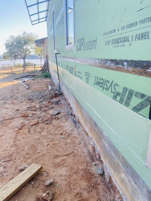 A building under construction; green sheathing covers the exterior. Dirt and gravel surround the base.