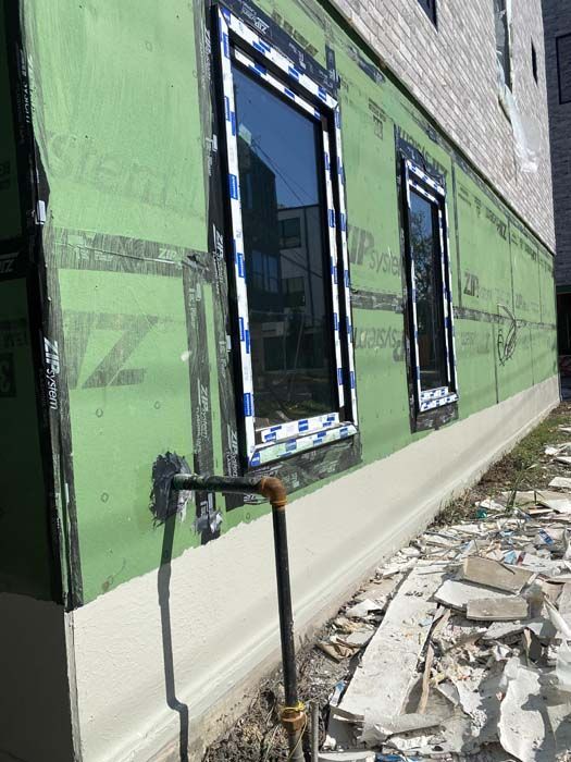 Exterior wall construction with windows, green sheathing, and a gas pipe.