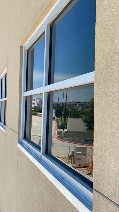 Exterior shot of a building with a large window reflecting a blue sky and surroundings.