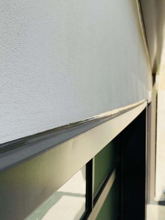 Close-up view of a dark metal frame against a textured light-colored wall, possibly a window or door.