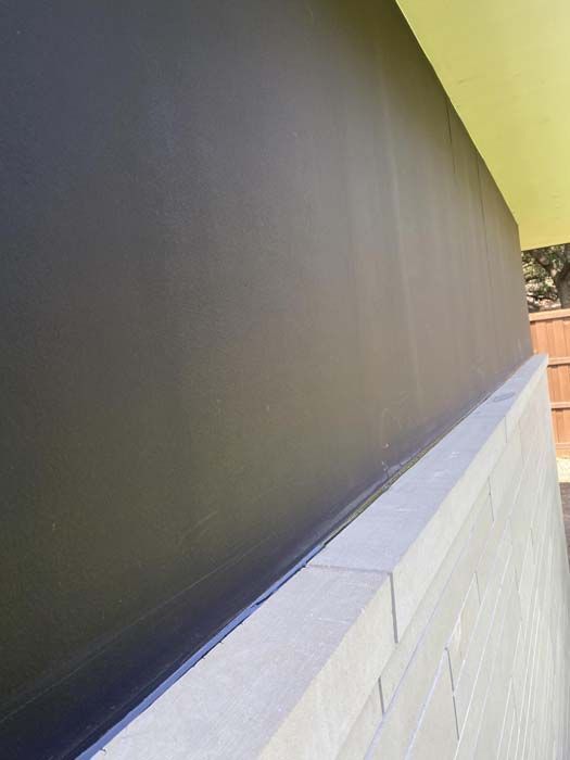 Black painted wall above a light brick wall, with a yellow overhang and wooden fence visible.