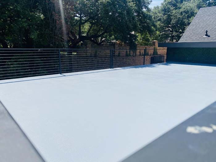 A light gray paved patio with a dark horizontal fence and greenery in the background.