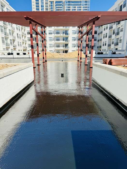 A glossy, dark surface reflects a pergola and apartment buildings on a sunny day.