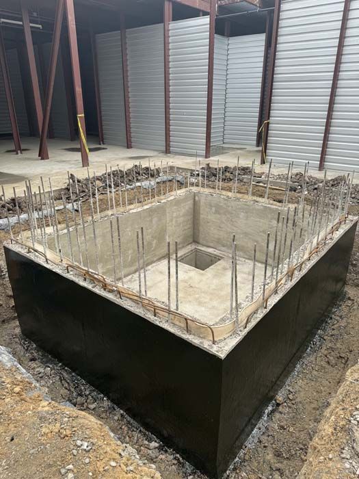 Concrete foundation with rebar, constructed outdoors. Surrounding metal structure and earth.