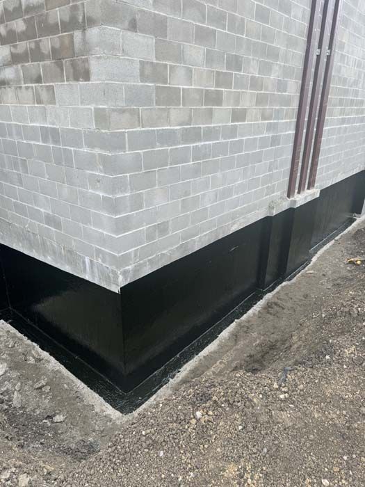 Gray cinder block building with a black waterproof coating on the foundation.