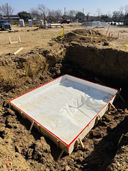 Construction site with a rectangular formwork in a dug-out hole, lined with white plastic.