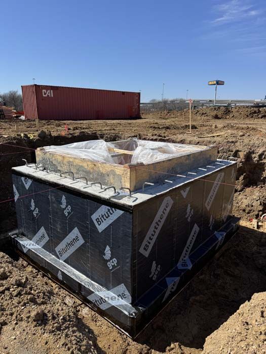 Construction site: Concrete foundation wrapped in black waterproof membrane, ready for the next phase.