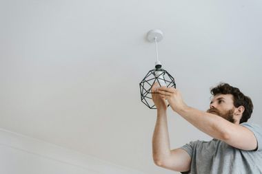 Man installing a light fixture on a white ceiling.