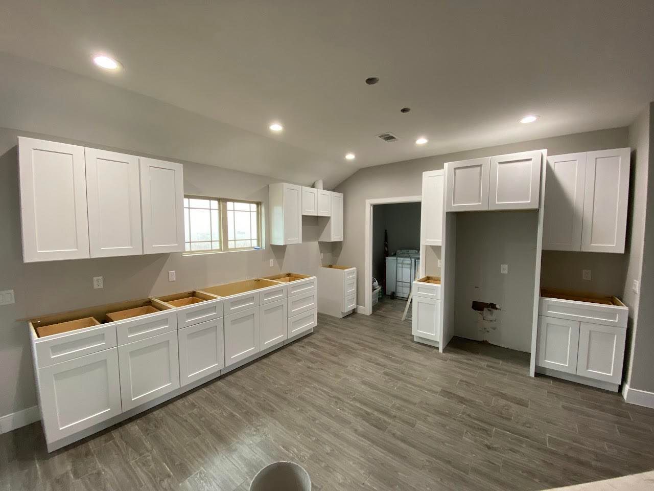 White kitchen cabinets installed in a room with wood-look flooring and recessed lighting.