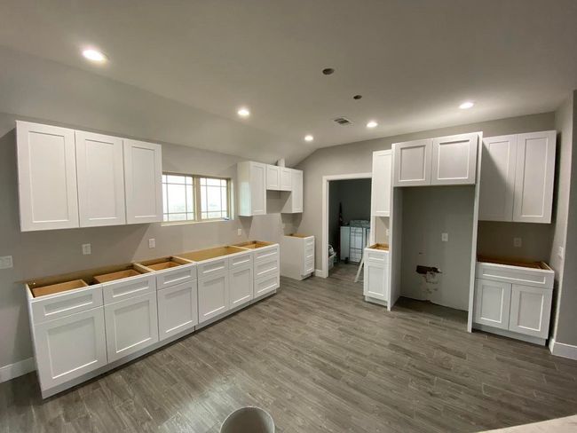 Empty kitchen with white cabinets, wood-look flooring, and bare countertops.