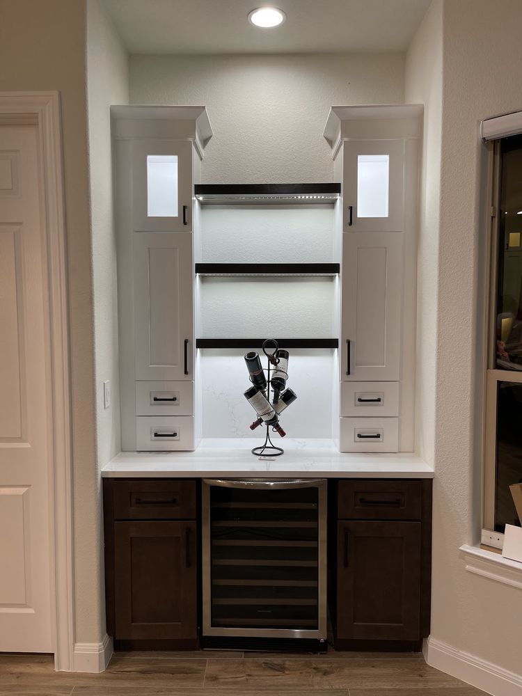 Wine bar with white and brown cabinets, wine cooler, and decorative wine rack.