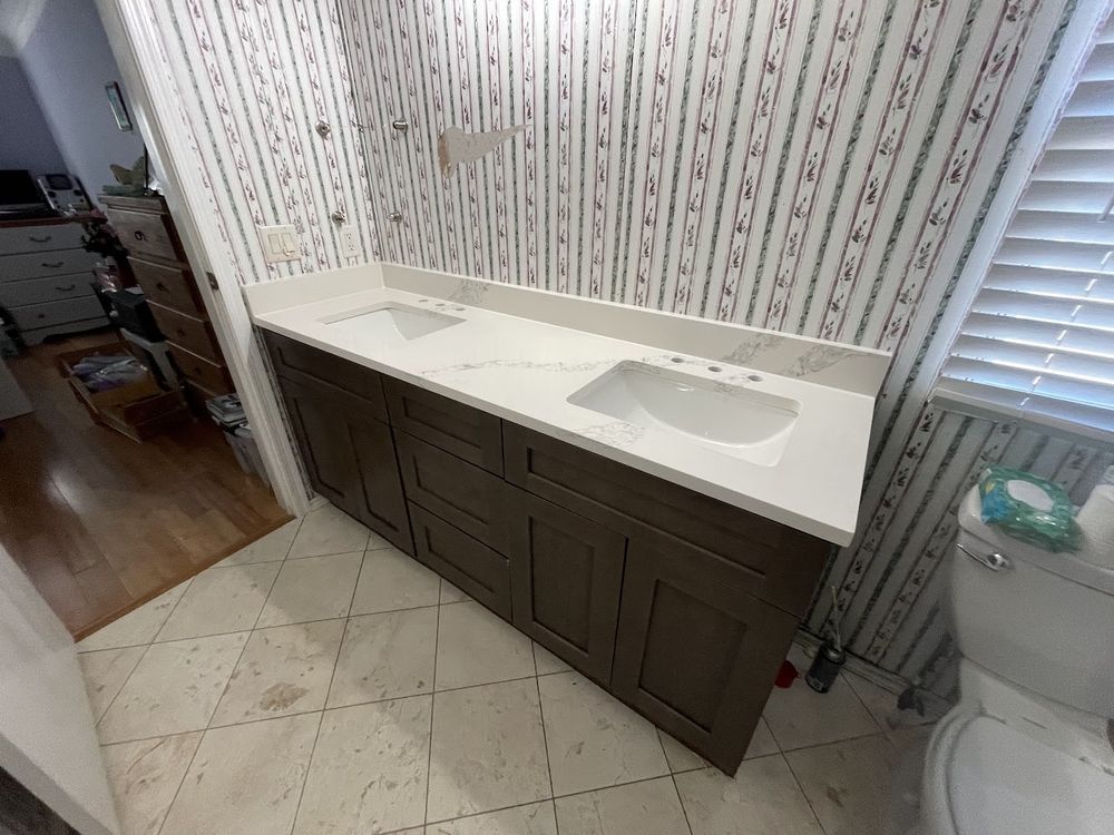 Bathroom with double sink vanity, gray cabinets, white countertop, patterned wallpaper, and tile floor.